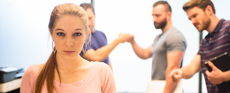 woman looking upset with three men in the back pointing at her and fist bumping hostile work environment