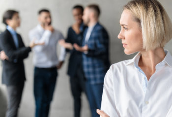 woman looking concerned while four men talk behind her sexism in the workplace