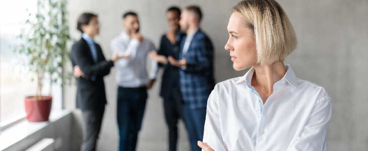 woman looking concerned while four men talk behind her sexism in the workplace