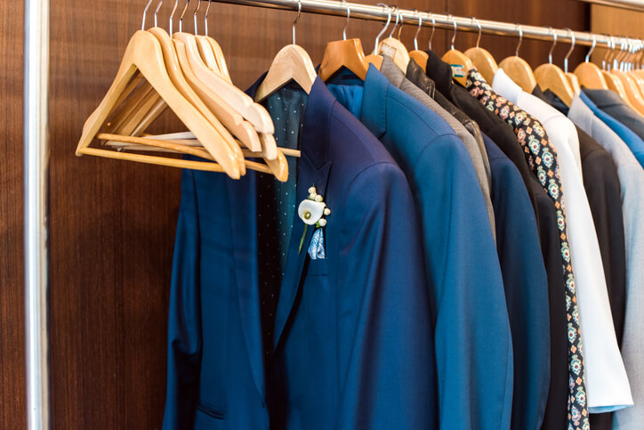 Several suit jackets hanging on hangers. The first jacket has a flower on the lapel. Concept of dress suit for groom on his wedding day.