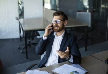 Corporate communication. Male entrepreneur talking on cellphone, sitting at workplace and having phone conversation, speaking with client discussing project, free space