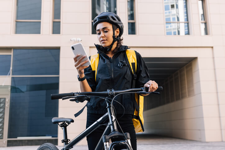 Courier with bike delivering food. Young courier checking delivery address on smartphone.