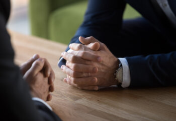 Clasped male hands of two businessmen negotiate at table, hr recruiter making hiring decision at difficult job interview, opponents dialogue debate, business confrontation challenge concept, close up