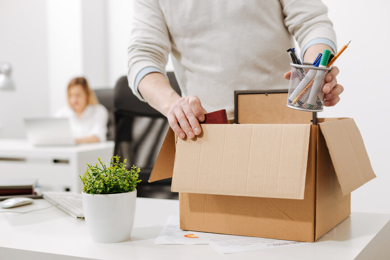 A person packs a box with their belongings on a desk, holding a pencil holder.