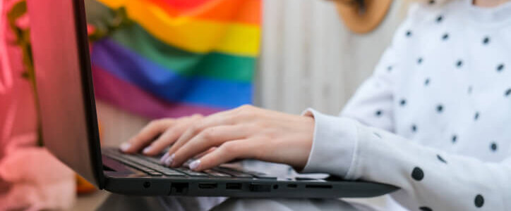 Woman on her laptop with gay pride flag in the background