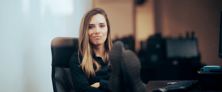 A young businesswoman leans back in her office chair with her feet on her desk.