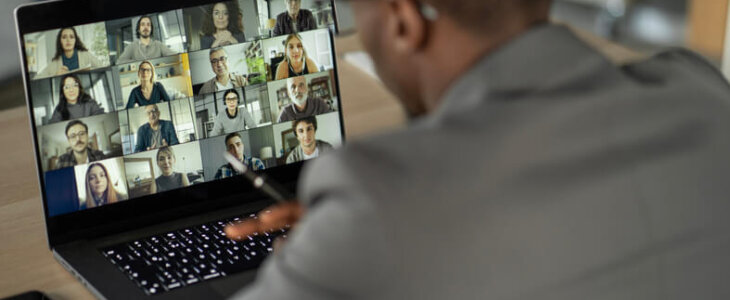 A man on a video call with a dozen other people on his laptop screen.