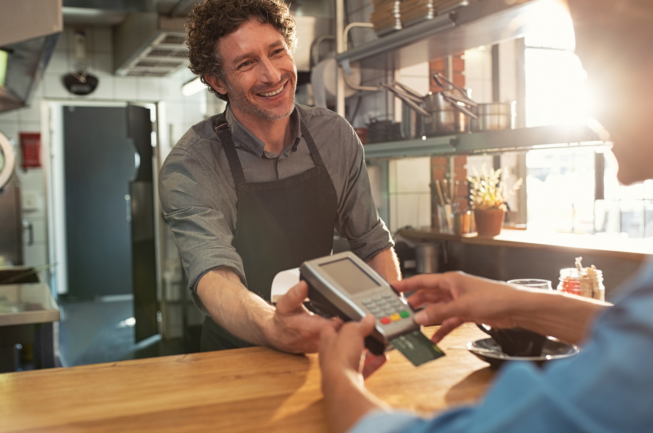 A smiling barista holds a card reader as a customer pays for an order.