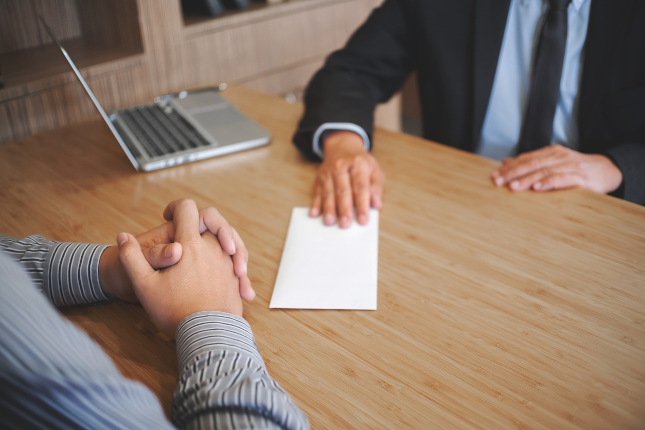 A businessperson handing a white envelope to another person across a desk.