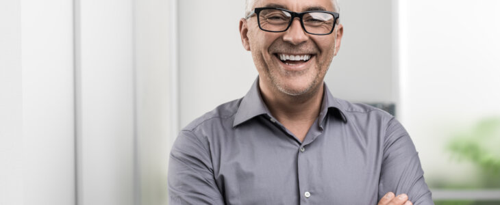 Confident businessman posing in the office with arms crossed, he is smiling at camera