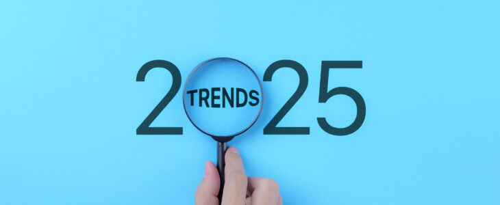 A hand holds a magnifying glass over the word "TRENDS" inside the number 2025.