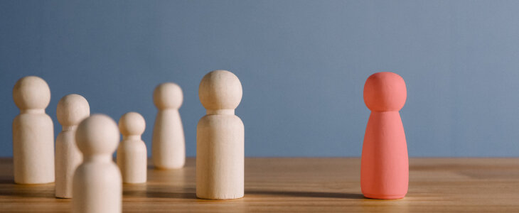 A red wooden figure standing apart from a small group of white wooden figures.