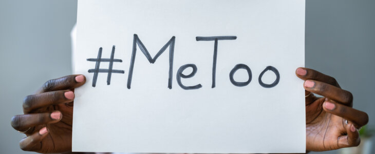 A Black woman holds a sign with the hashtag #MeToo written on it.
